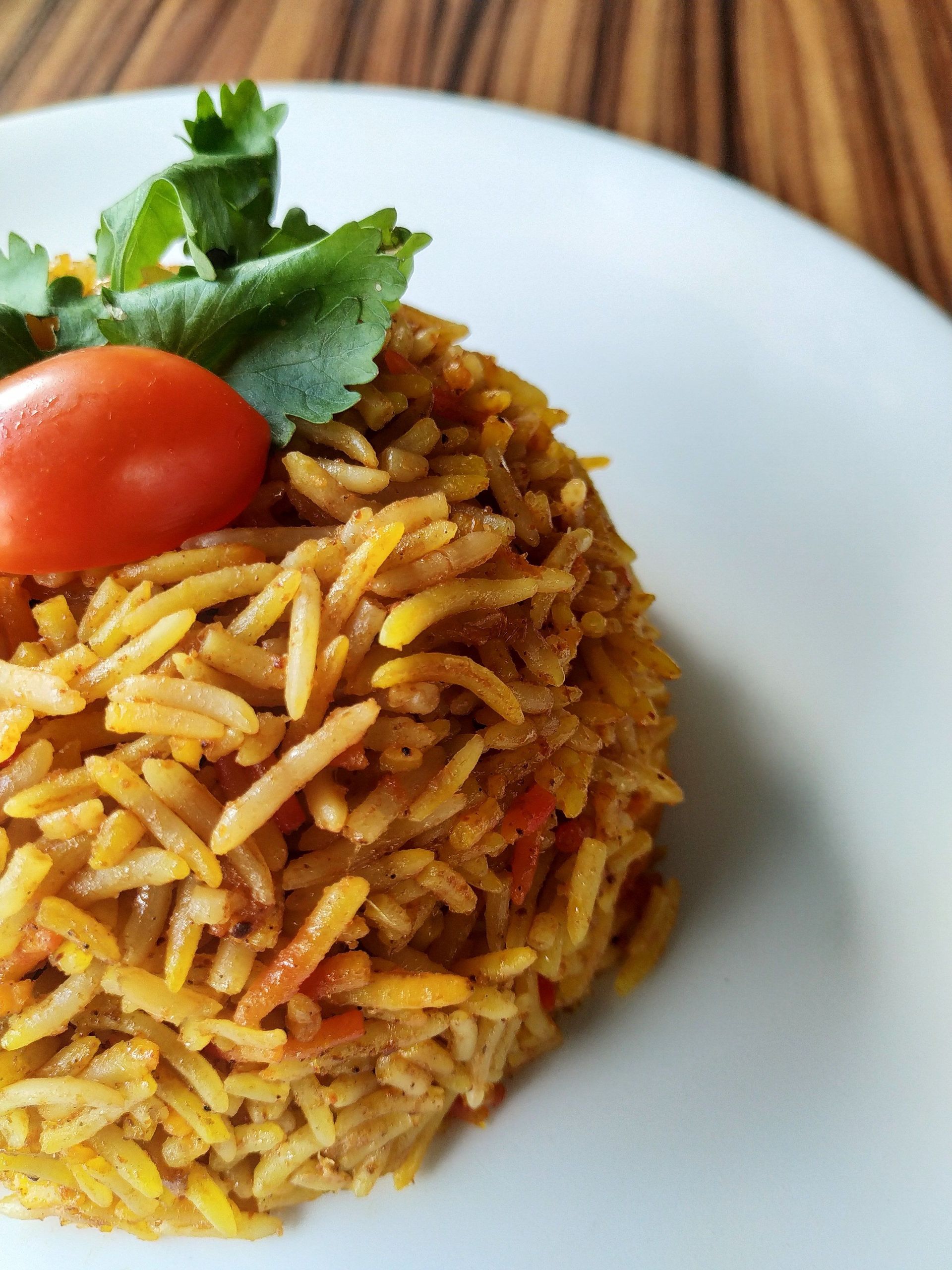 Delicious biryani rice garnished with tomato and coriander on a white plate. Perfect for food lovers.