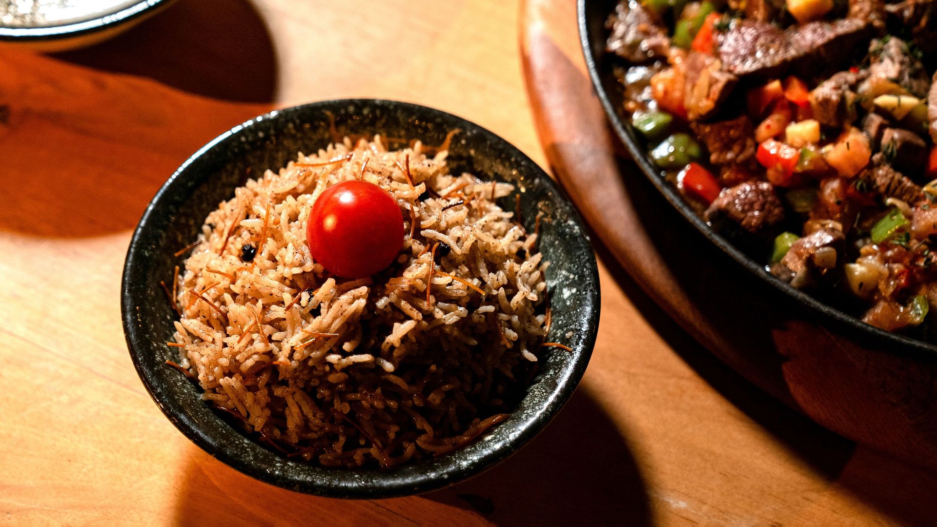 Appetizing rice dish topped with a cherry tomato, next to a colorful side dish.