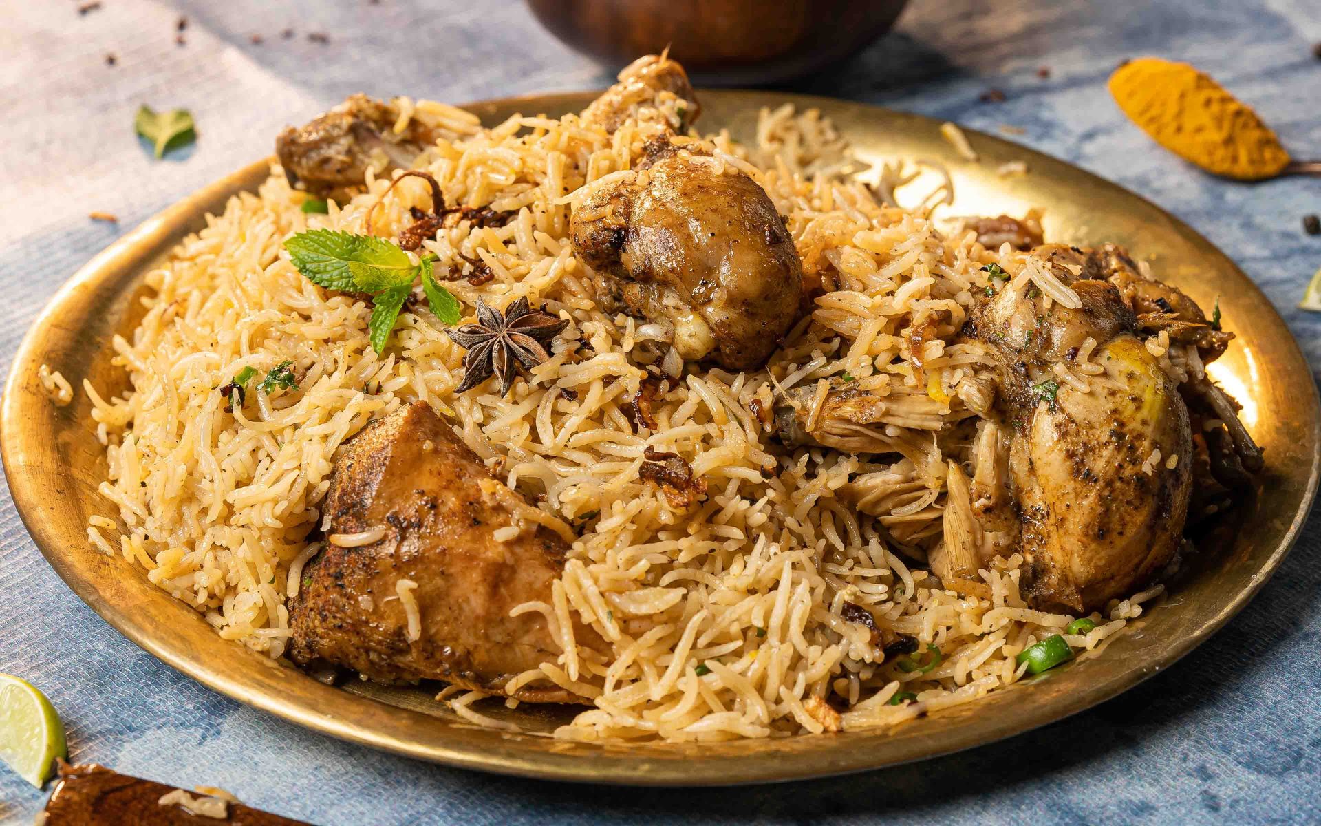 Close-up of aromatic chicken biryani served on a brass plate with garnishes, showcasing Indian culinary art.
