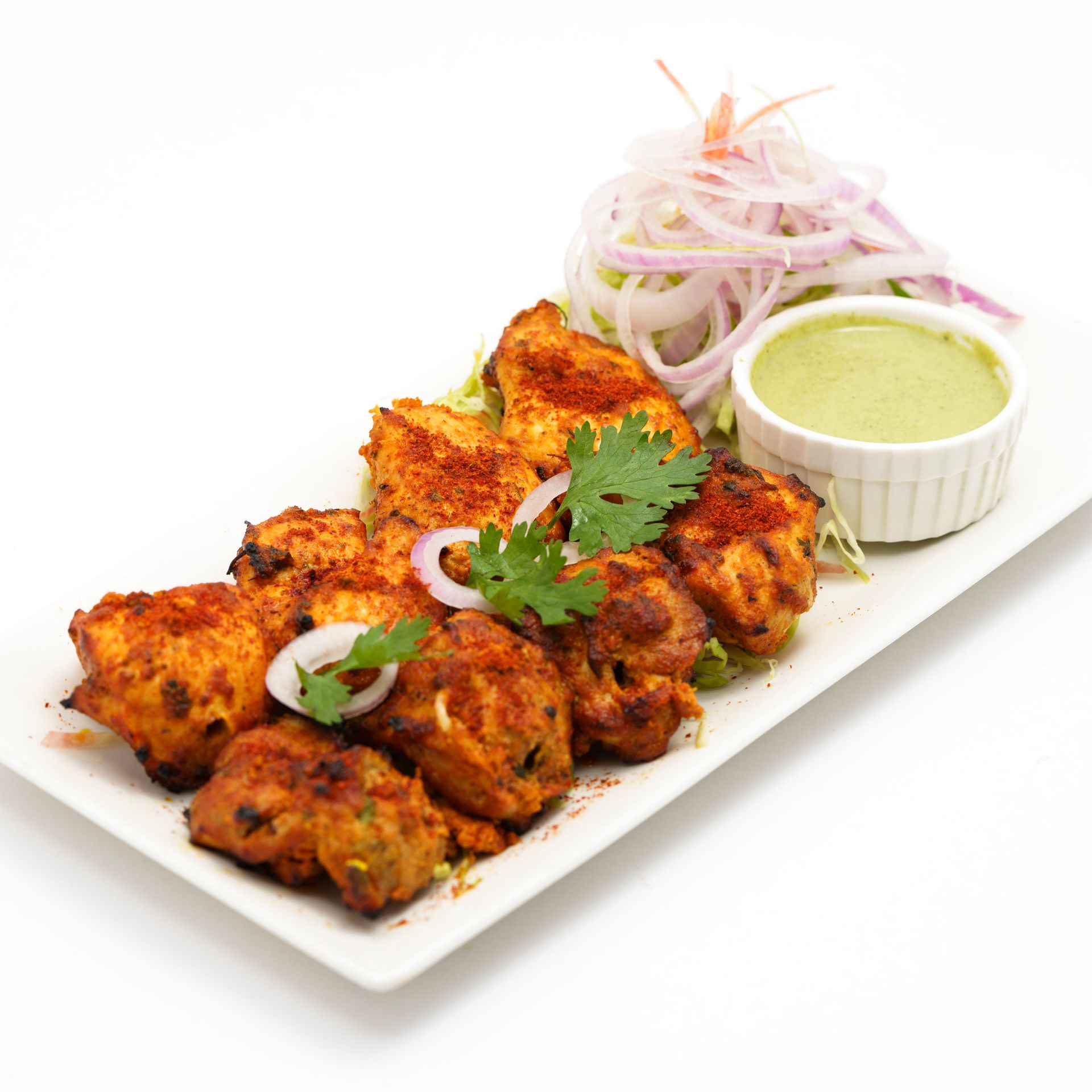 Delicious spicy tandoori chicken served with mint chutney and onion salad on a white platter.