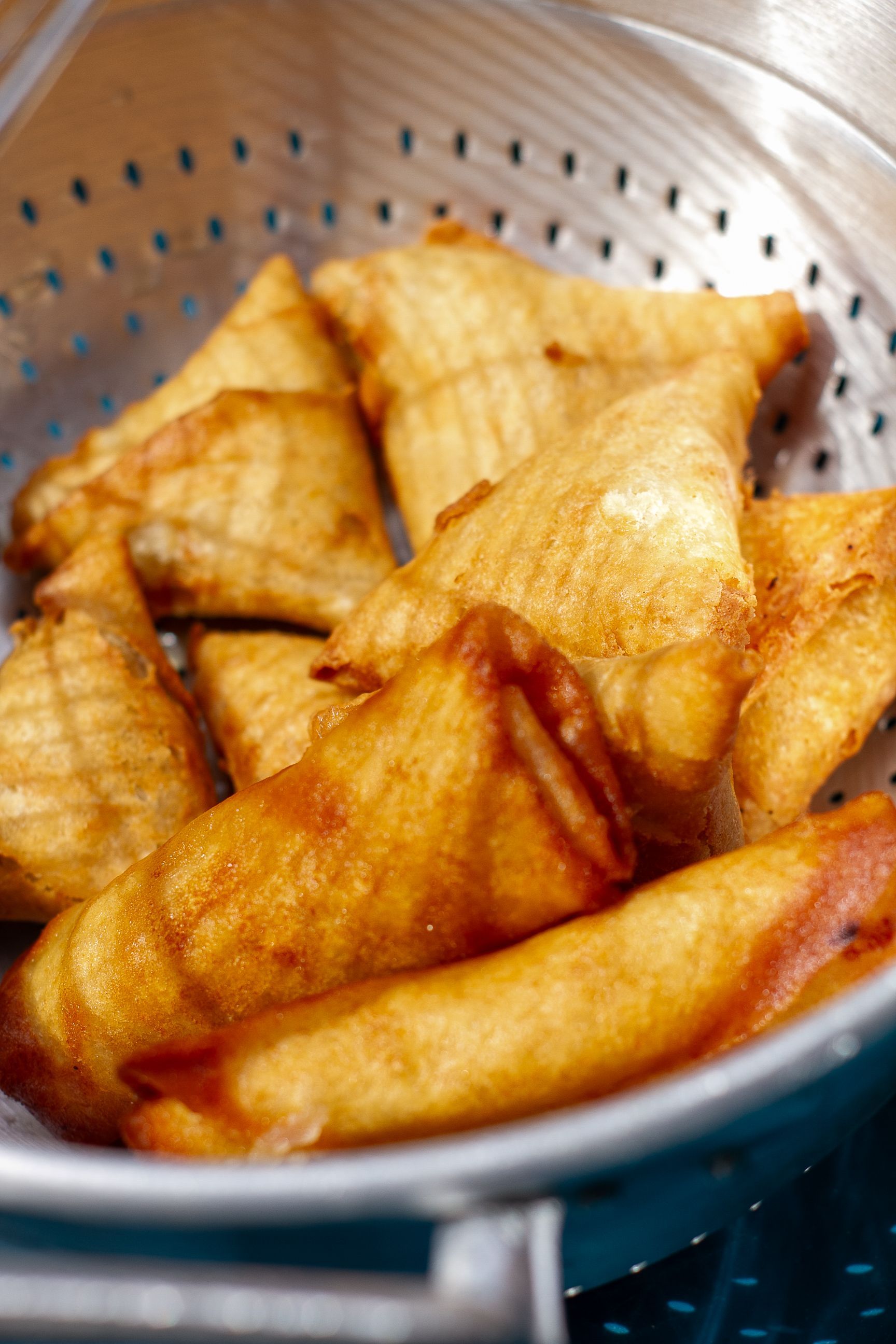 Delicious homemade samosas freshly fried and placed in a colander, ready to eat.